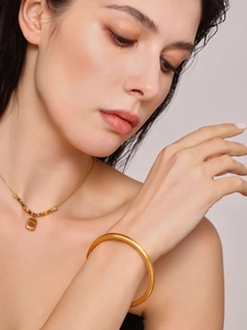 Close-up of minimalist 18K gold plated thick hollow bangle and engraved logo necklace