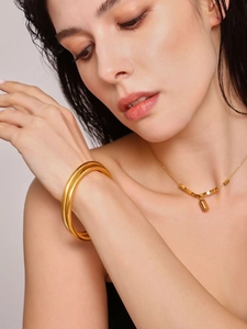 Close-up of minimalist 18K gold plated thick round bangle and matching geometric necklace