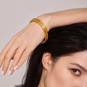 Minimalist double-band gold bangle in matte finish worn by a female model on a soft background
