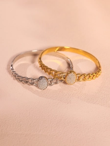 Detail of gold and silver NK chain bracelets with oval zircon buckle on pink texture