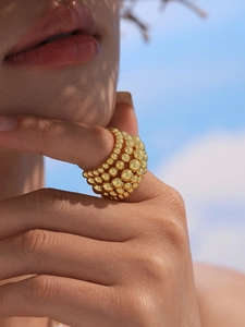 Macro detail of chunky gold multi-layer beaded ring on finger against blue sky background