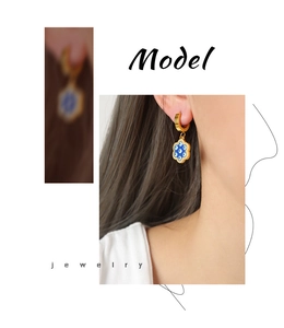 Nahaufnahme goldener Creolen mit blau-weißem Emaille-Blumenanhänger am Ohr des Models
