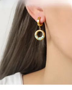 Detailaufnahme eines Models mit goldenen Evil-Eye-Ohrringen und blauem Emaille-Schmuck