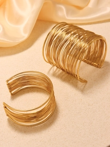 Dettaglio di bracciali multistrato in acciaio inossidabile dorato su trama beige