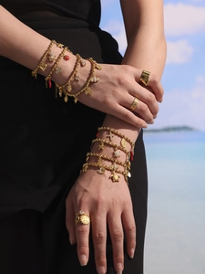 Detailed view of layered gold-plated bracelets and rings with various dainty charms