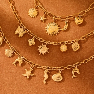 Gold stainless steel bracelet with sun and sea-themed charms on textured background