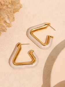 Detailed close-up of gold-plated triangle earrings with white enamel on a stone surface