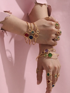 Close-up of stacked gold-plated bracelets and rings with colorful square crystals on hands