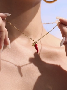 Macro detail of red chili and clover pendants on 18k gold plated stainless steel necklace