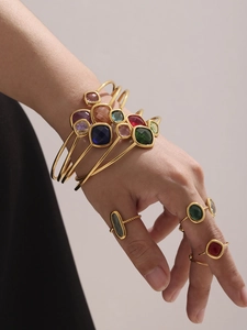 Detail of stacked gold bangles with colorful gemstones and rope textured rings on model hand