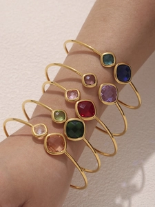 Close-up of gold-plated open bangles with colorful square gemstones on a model's wrist