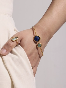 Detail of gold-plated bangle with colorful square gems and matching twisted ring