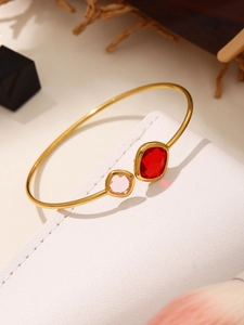Detail of gold-plated bangle featuring square-cut red and pink crystals on white leather