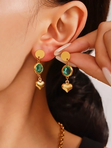 Primer plano de pendientes colgantes dorados con piedras verdes y colgantes de corazón