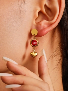 Detailed close-up of golden hollow heart drop earrings with red round stone accents