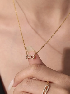 Gros plan du pendentif infini avec zircons et bague dorée assortie sur le mannequin