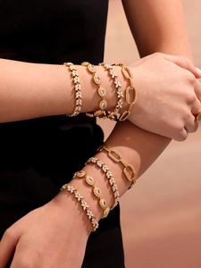 Close-up of layered gold bracelets with leaf and water drop zircon charms on a wrist