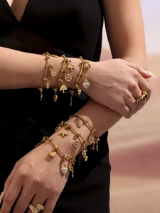 Primer plano de pulseras de acero dorado con trébol y dijes de corazón en la muñeca