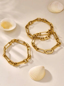 Nahaufnahme goldener Gliederketten mit einer Muschel auf beigefarbenem Hintergrund