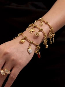 Detalle de pulseras con dijes chapadas en oro de 18K y anillo cruzado con diamantes