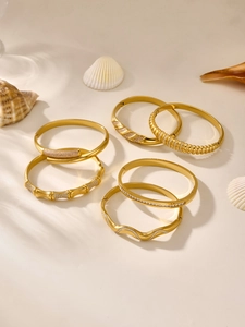 Close-up of six gold-plated bangle bracelets with cubic zirconia on a luxury shell surface