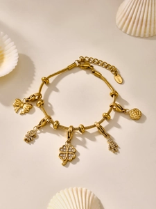Detalle de una pulsera de acero inoxidable dorado con dijes de trébol y oso