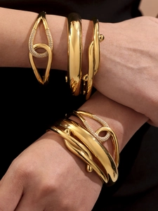 Close-up of stacked gold-plated bangles with irregular twisted design and crystal accents