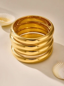 Close-up of stacked chunky gold plated bangles with shells in a minimalist setting