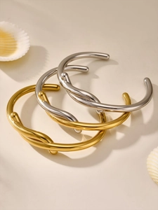 Detailed close-up of three polished metal twisted cuff bracelets on a sandy surface