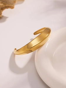 Vista detallada de un brazalete ancho dorado en forma de C con textura pulida sobre porcelana