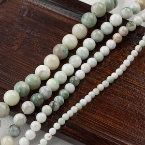 Natural jade beads in mixed green tones on a dark wood background for DIY jewelry