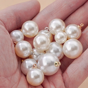 Creamy white ABS imitation pearl pendants with gold hooks held in hand for size reference