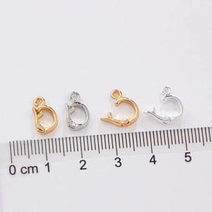 Dolphin-shaped gold and silver jewelry clasps shown with a metric ruler for size