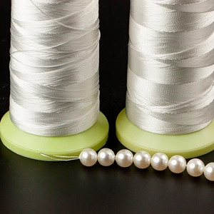 Macro view of white braided polyester beading thread with glossy pearls on dark background