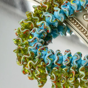 Makroaufnahme von Lampwork-Glasperlen mit Wellenrand und bunten Wirbeln auf Spiegelfläche