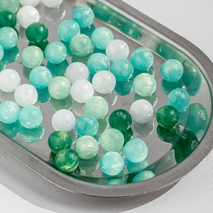 Detailed view of green and white cat eye beads for DIY jewelry making in a metal tray