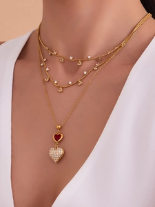 Primo piano di collane d'oro a tre strati con pendente a cuore rosso e cristalli su una modella
