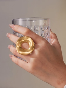 Close-up of a chunky gold dome ring with a mirror finish on a model holding a glass