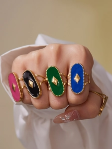 Gros plan de quatre bagues ovales en émail coloré rose, noir, vert et bleu sur une main de mannequin