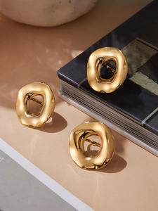 Detail shot of irregular gold wave rings on a minimalist beige and ceramic background