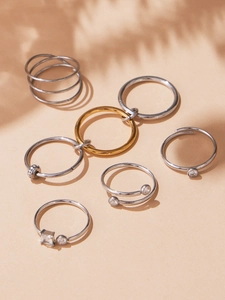 Detailed stack of seven gold and silver rings with zircon stones on warm beige background