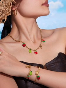 Detailed shot of fruit-themed enamel strawberry and watermelon charms on gold bead necklaces