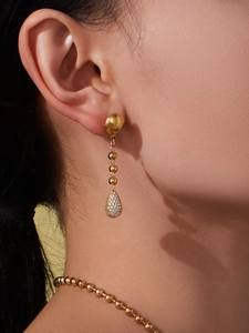 Close-up of golden stainless steel drop earring with zircon on a model for jewelry set