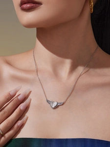 Detail einer silbernen Halskette mit Herz-Flügel-Anhänger und Zirkonia am Hals eines Models