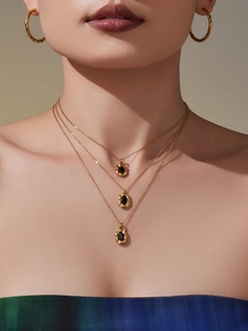 Close-up of a three-layer gold necklace with black stone and twisted hoop earrings