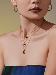 Detail of layered gold necklaces with oval black gemstone pendants and twisted hoop earrings