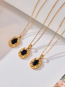 Three gold necklaces with oval black zircon pendants on a minimalist white platform
