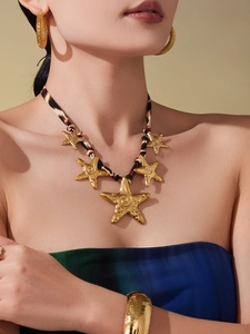 Close-up of golden starfish charms on a leopard print cord necklace with hammered bangles