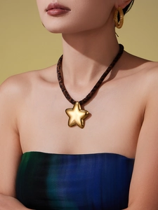 Detail of a gold star pendant necklace with leopard print cord on a model with earrings