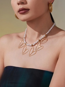 Dettaglio della collana di perle con grandi pendenti a cuore dorati su modella